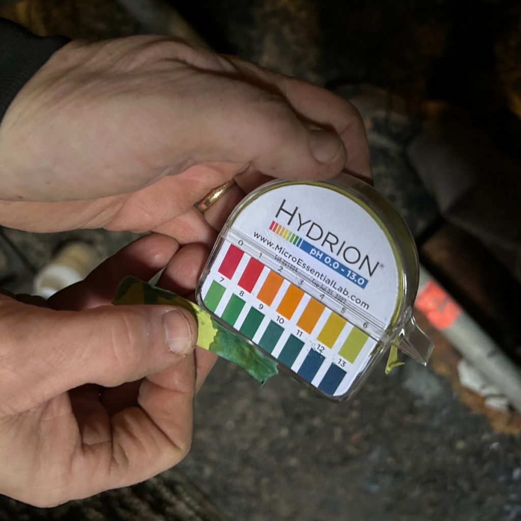 This shows a person holding a Hydrion pH test kit and comparing a used pH test strip to the color chart.